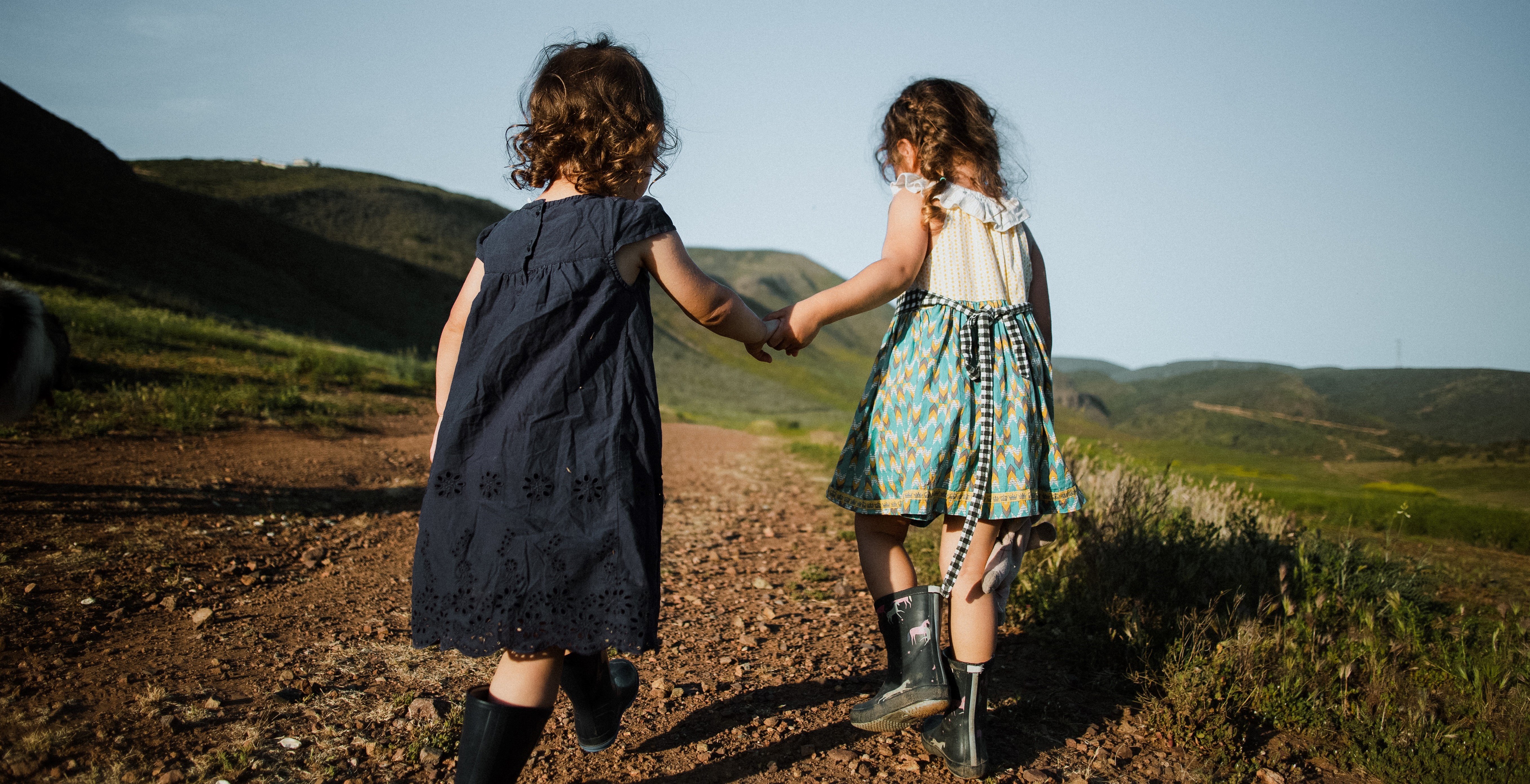 two small children in rain boots holding hands and walking