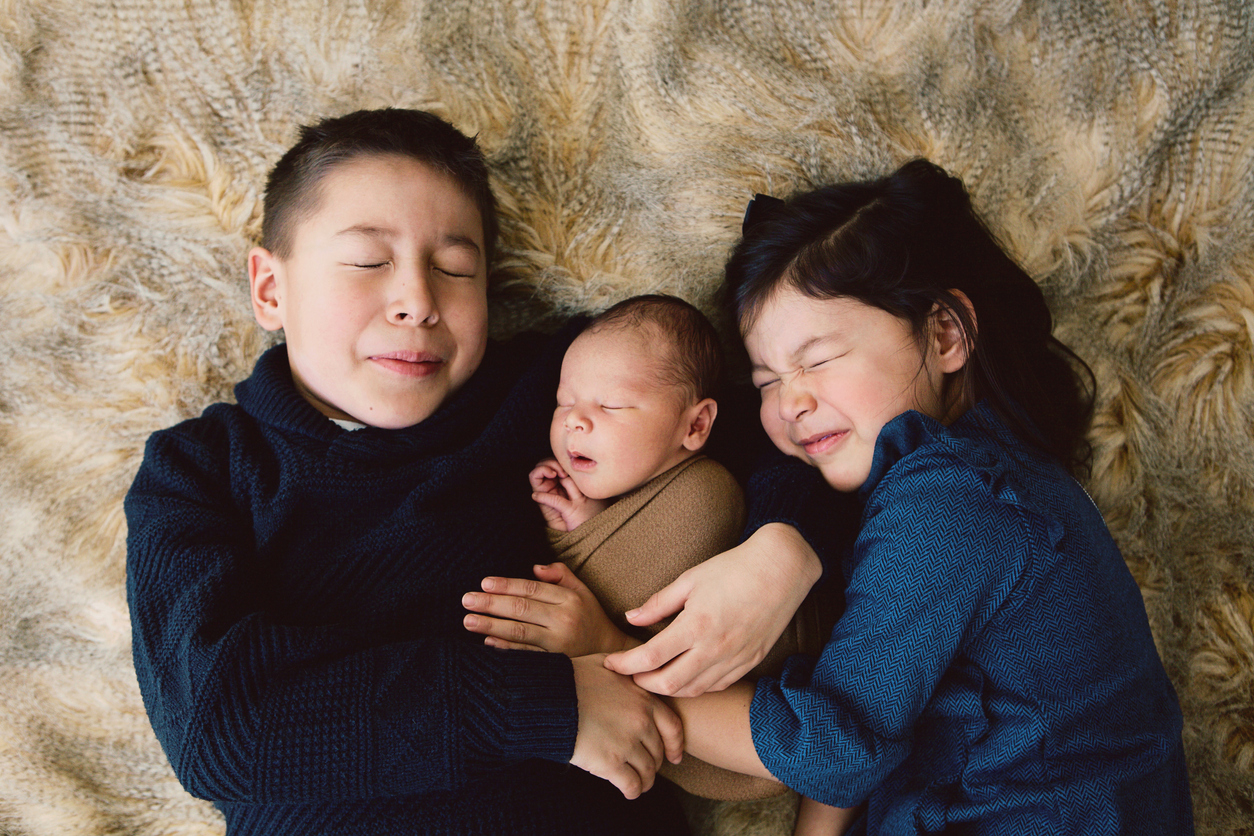 Indigenous siblings cuddling newborn