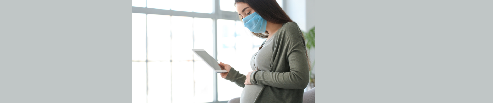 pregnant woman wearing a mask looking at her tablet