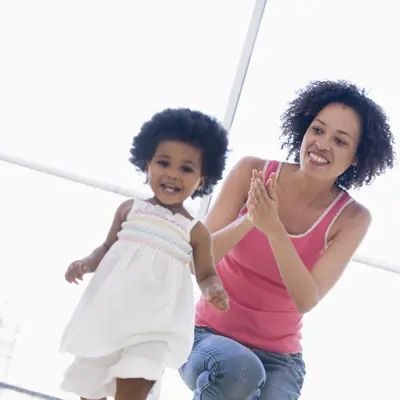 Mom smiling as she watches her toddler daughter take some steps