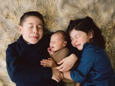3 siblings - 2 children and a newborn - snuggling on bed